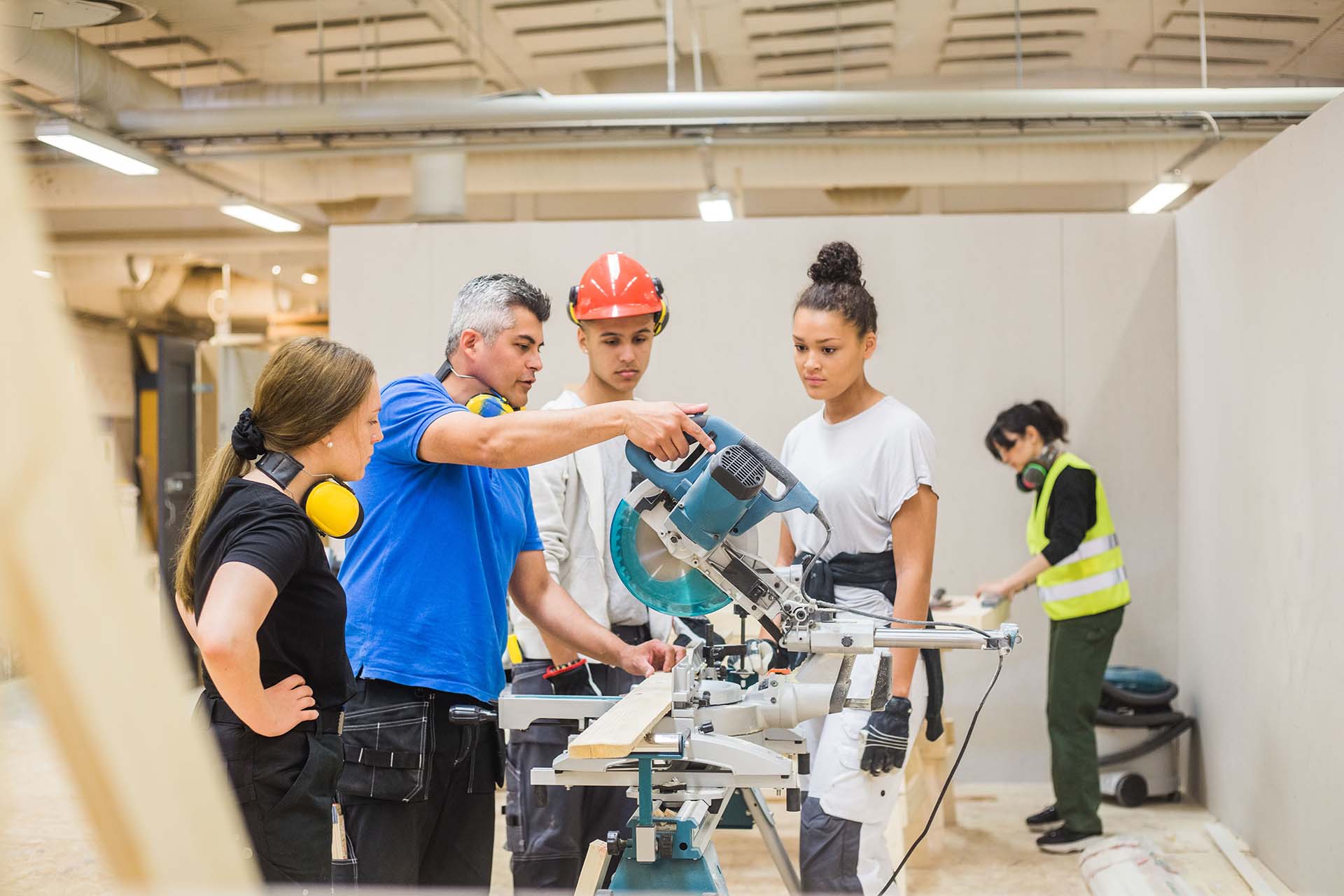 Trainees Watching Confident Male Carpenter Cutting With Electric Saw In Workshop Trainees Watching Confident Male Carpenter Cutting With Electric Saw In Workshop