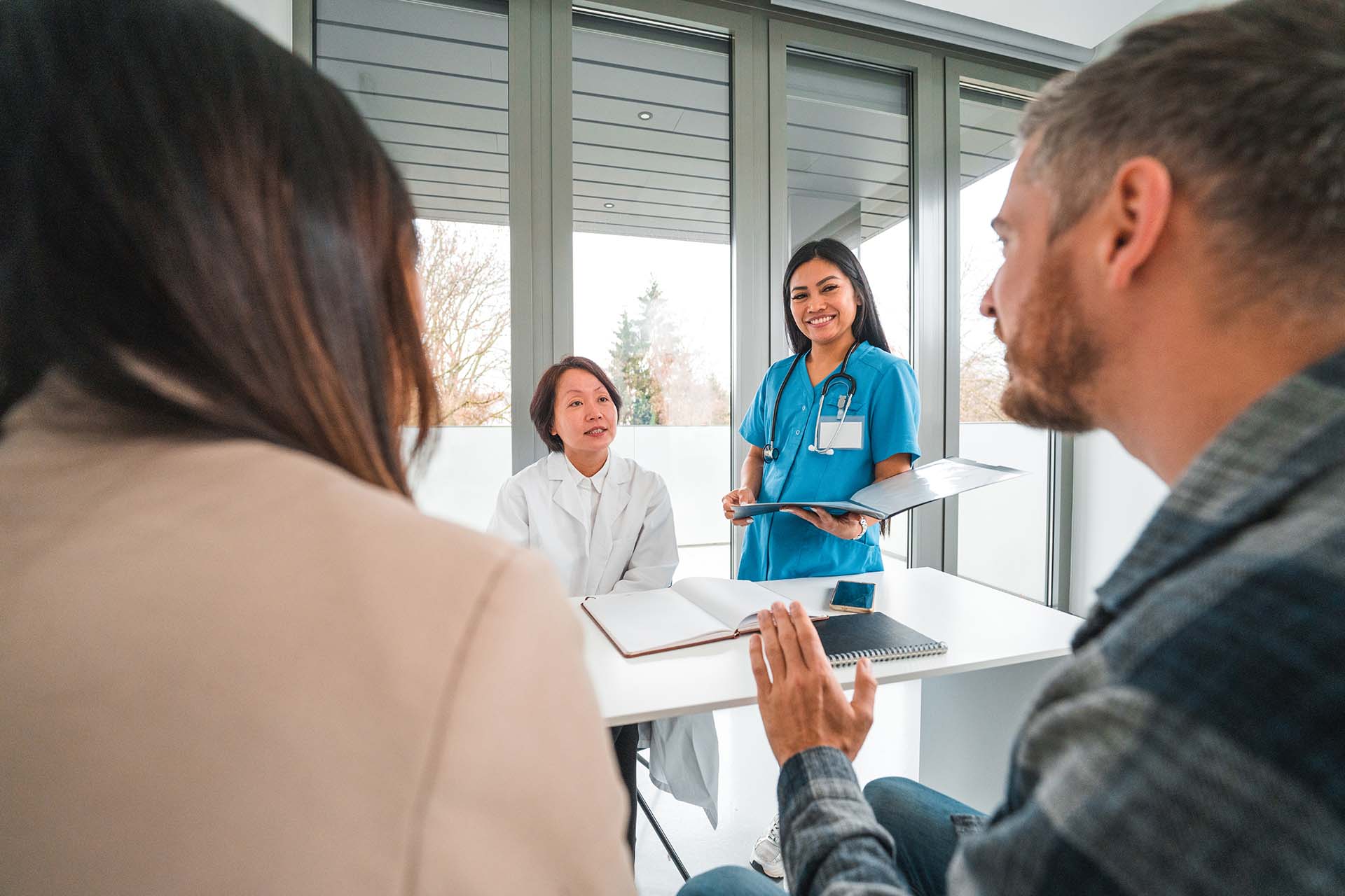 Cheerful Asian females working in a medical centre. They are discussing with a young mixed race couple. They are happy and smiling.