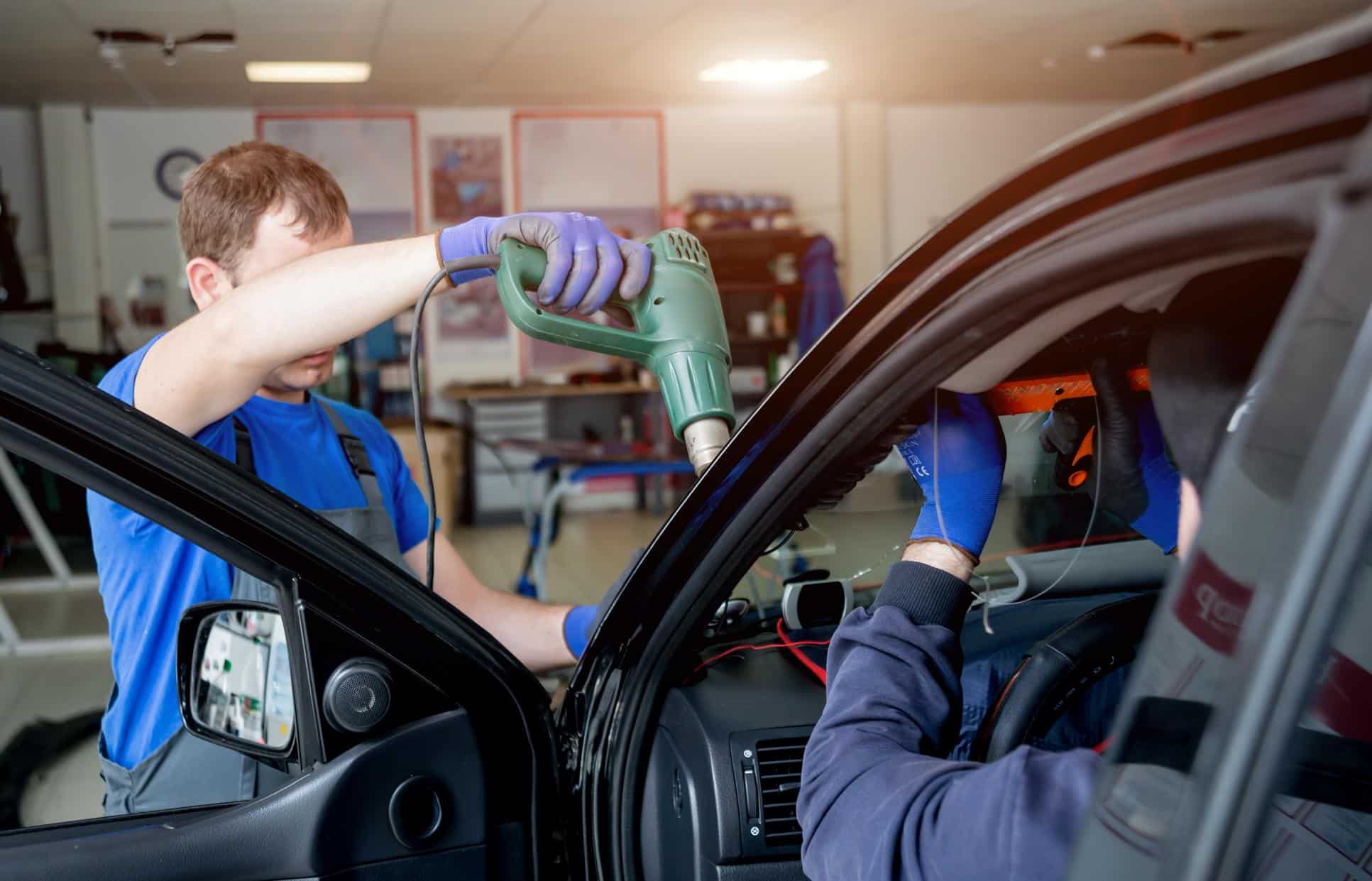 Automobile special workers remove old windscreen or windshield of a car in auto service station garage. Background