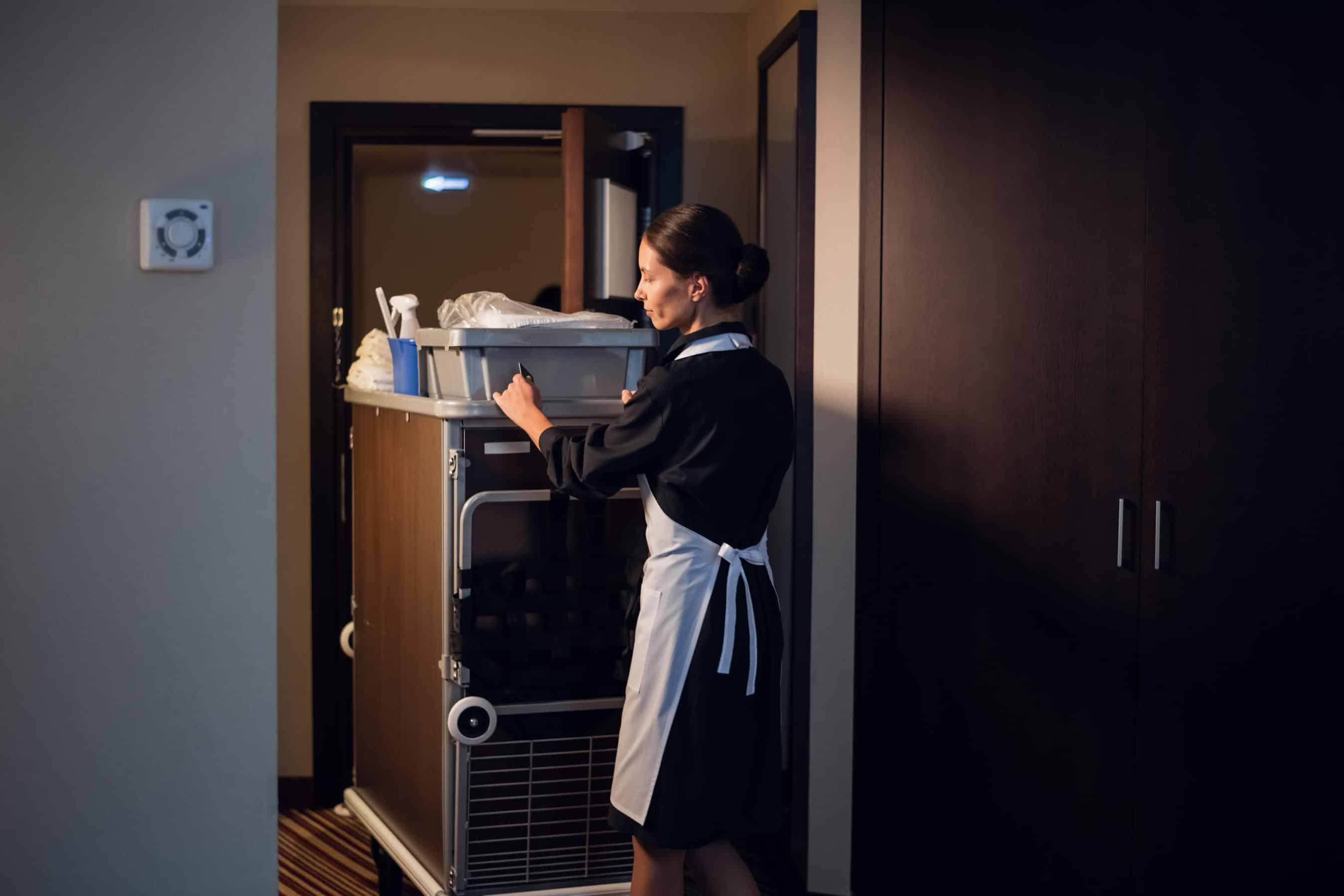 Hotel service. A female housekeeping worker with a trolley entering a room.