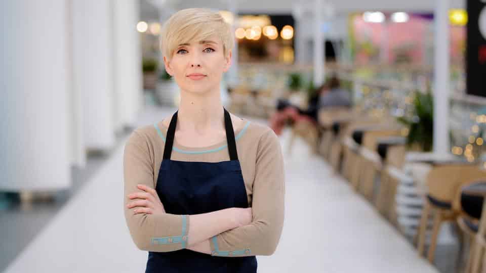 Mature adult middle aged 40s woman lady restaurant cafe worker looking at camera posing crossing arms female waitress saleswoman in apron standing at work space profession concept. Small business. High quality 4k footage