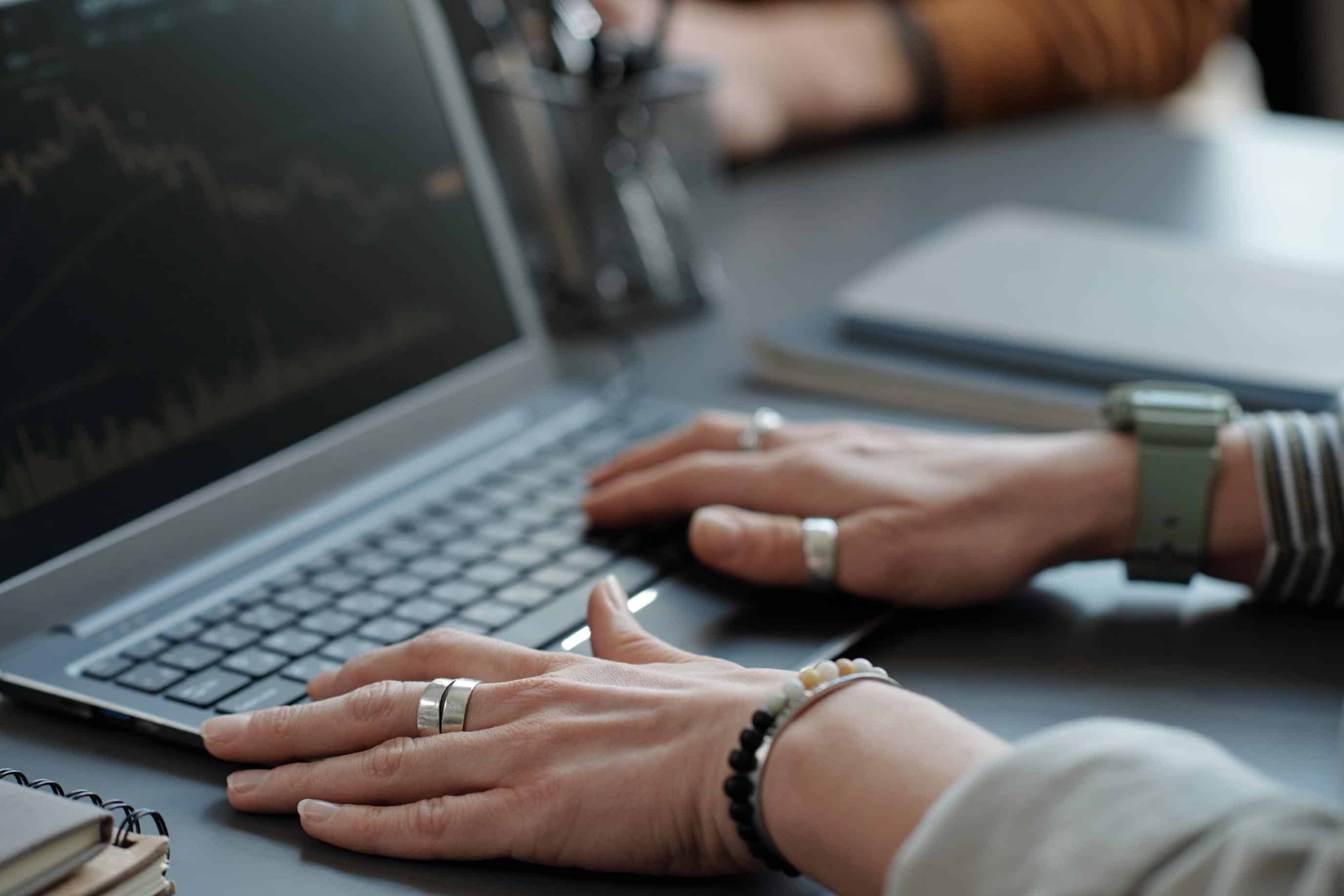 Hands of female trader or broker touching laptop keyboard while sitting by workplace in office, analyzing financial data and creating graph