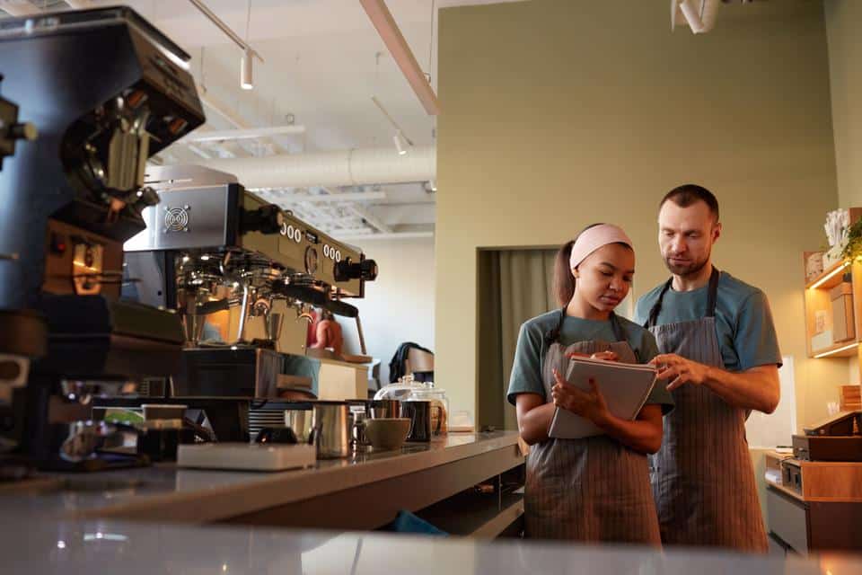 Waiters At Bar In Cafe Waist up portrait of two young waiters wearing aprons while doing inventory in cafe or coffee shop, copy space